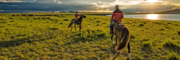 Photo of two people on horseback in the vast and empty Mongolian steppe.