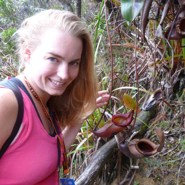 A woman smiles at the camera as she examines carnivorous plants in the wild.