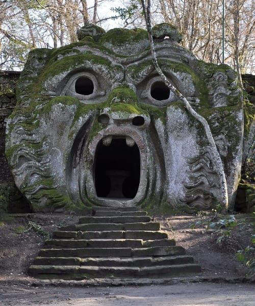 from the Garden of Monsters in Bomarzo: a monstrous face constructed in stone, covered in moss, steps lead into the cave of its gaping mouth. 