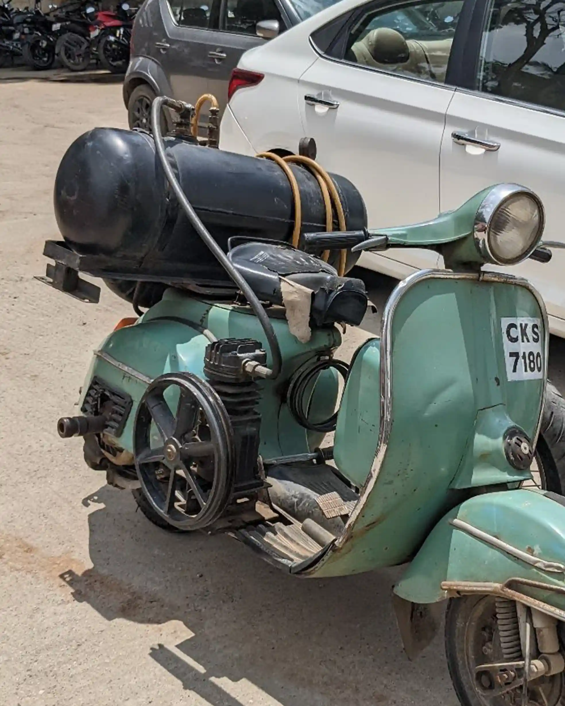 Green Chetak scooter modified into a mobile air compressor unit with a black pressure tank and belt-driven pump system.