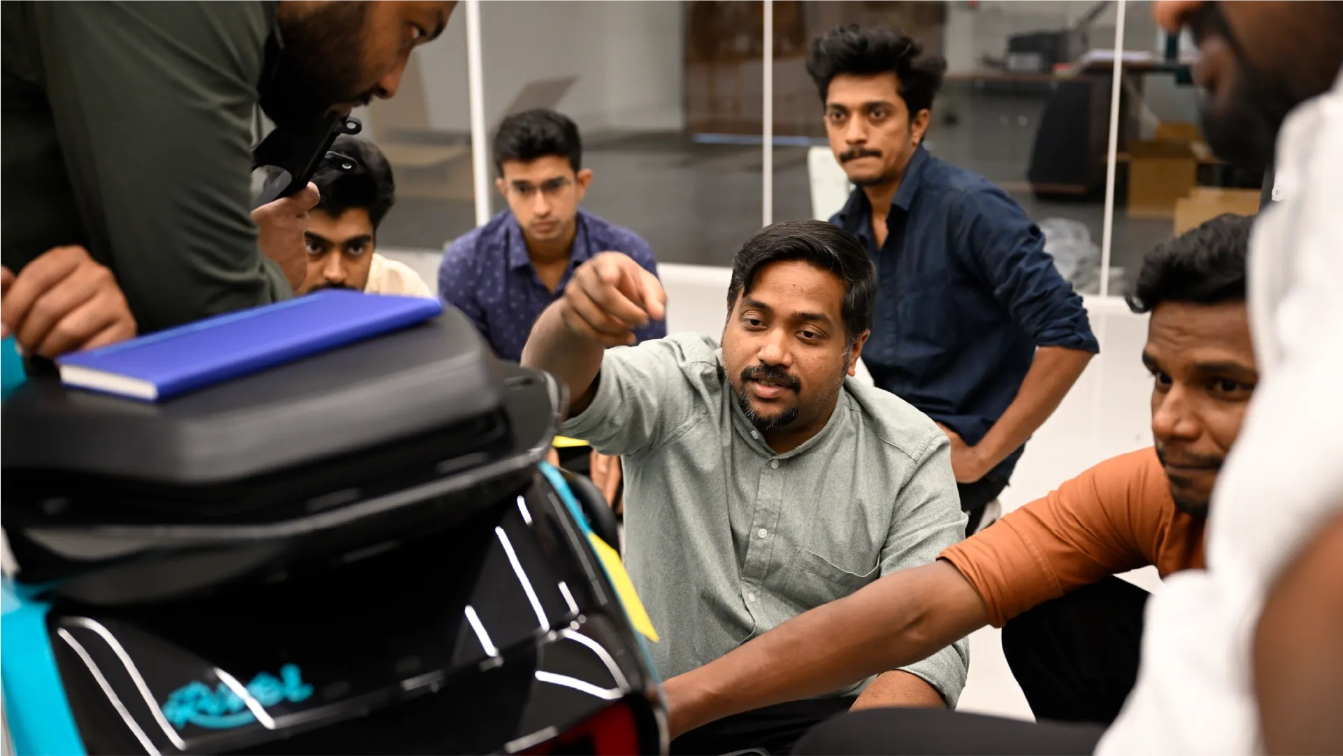 Vipin surrounded by industrial designers, pointing at the side pannier on the scooter prototype.