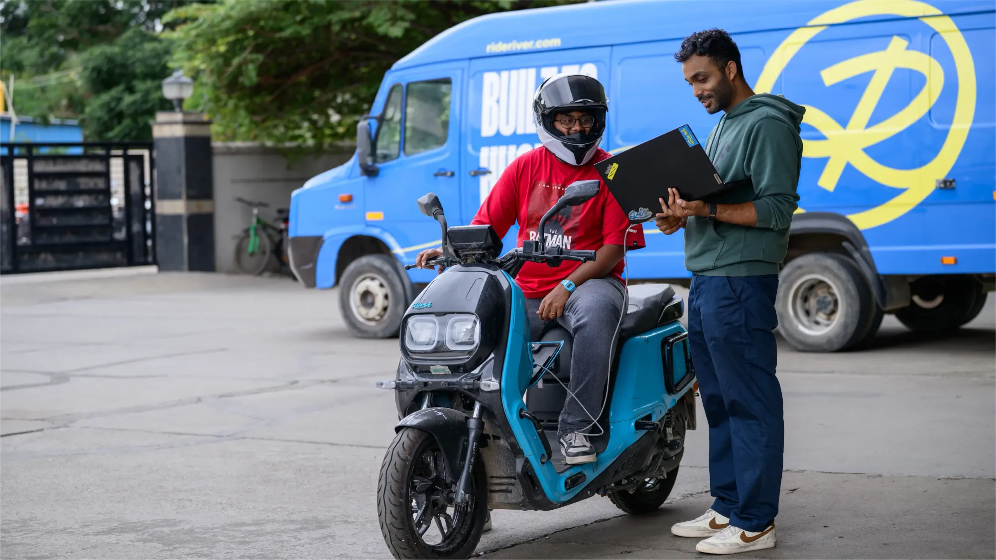 Ranjan reads vehicle updates on a laptop with a colleague seated on a Summer Blue Indie.