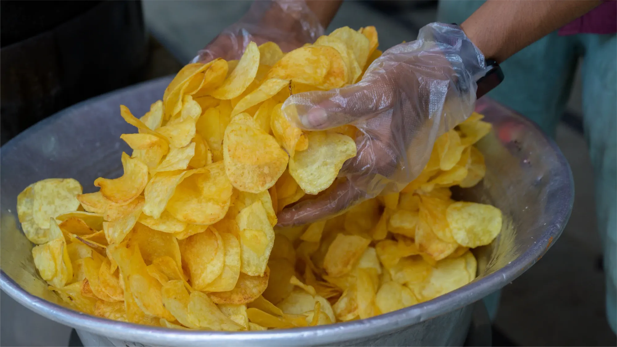An employee delicately holding in his hands a large portion of fresh potato chips straight out of the hot oil