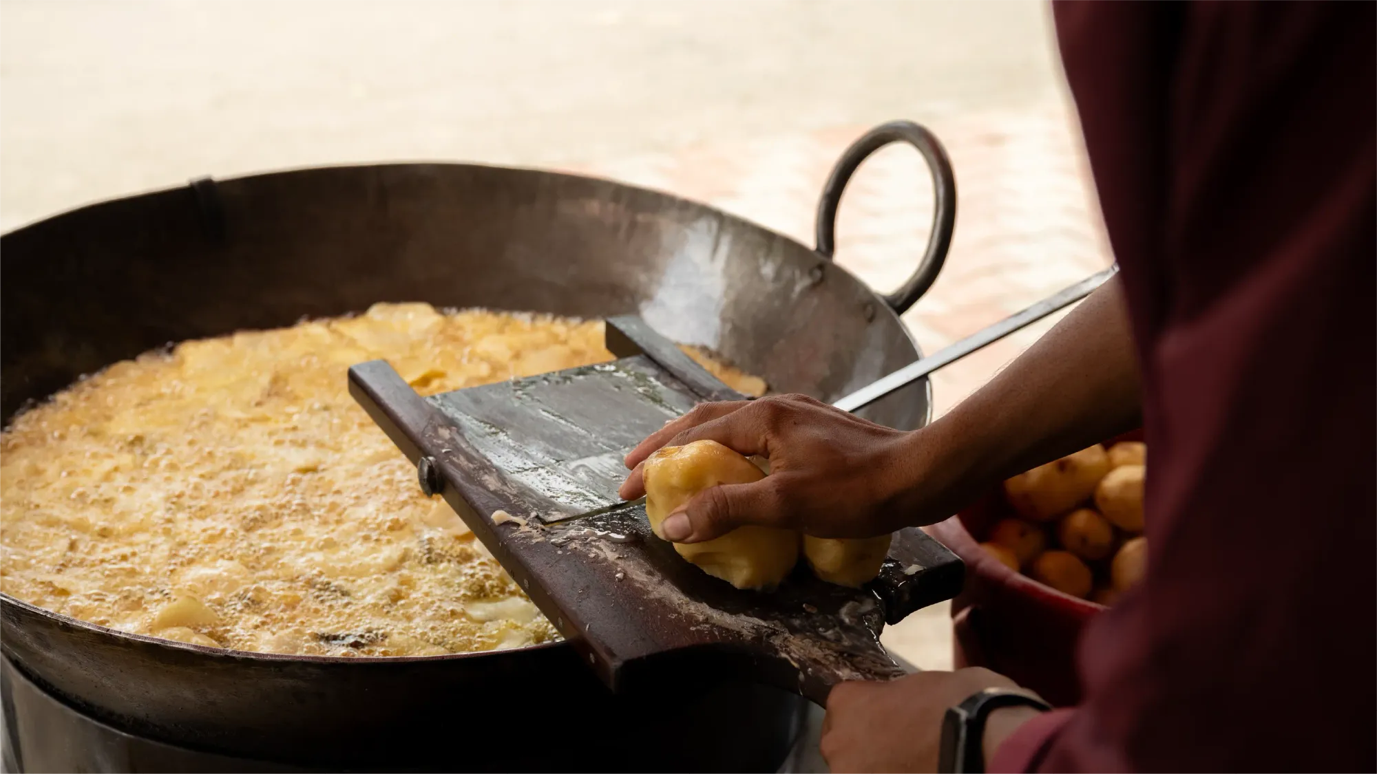 Boiled potato being sliced into thin chips, over a large pot of hot oil