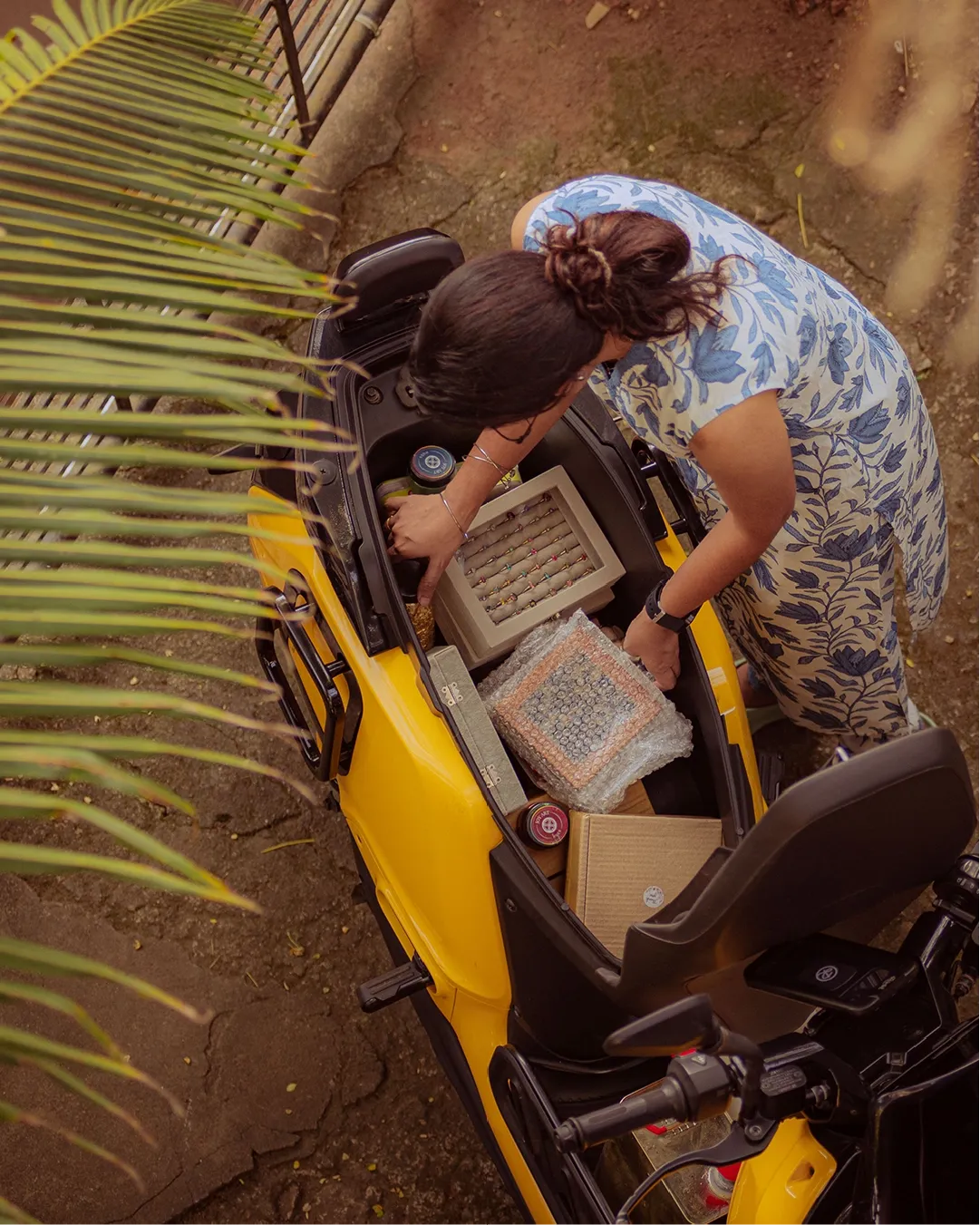 Top-down view of someone packing crafts, boxes, and jars into a Spring Yellow Indie's underseat storage.
