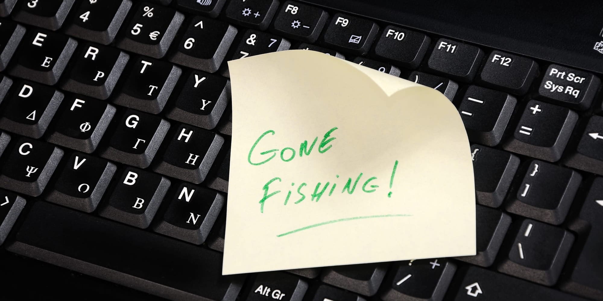 A sticky note reading “Gone Fishing!” sits on top of a black computer keyboard.