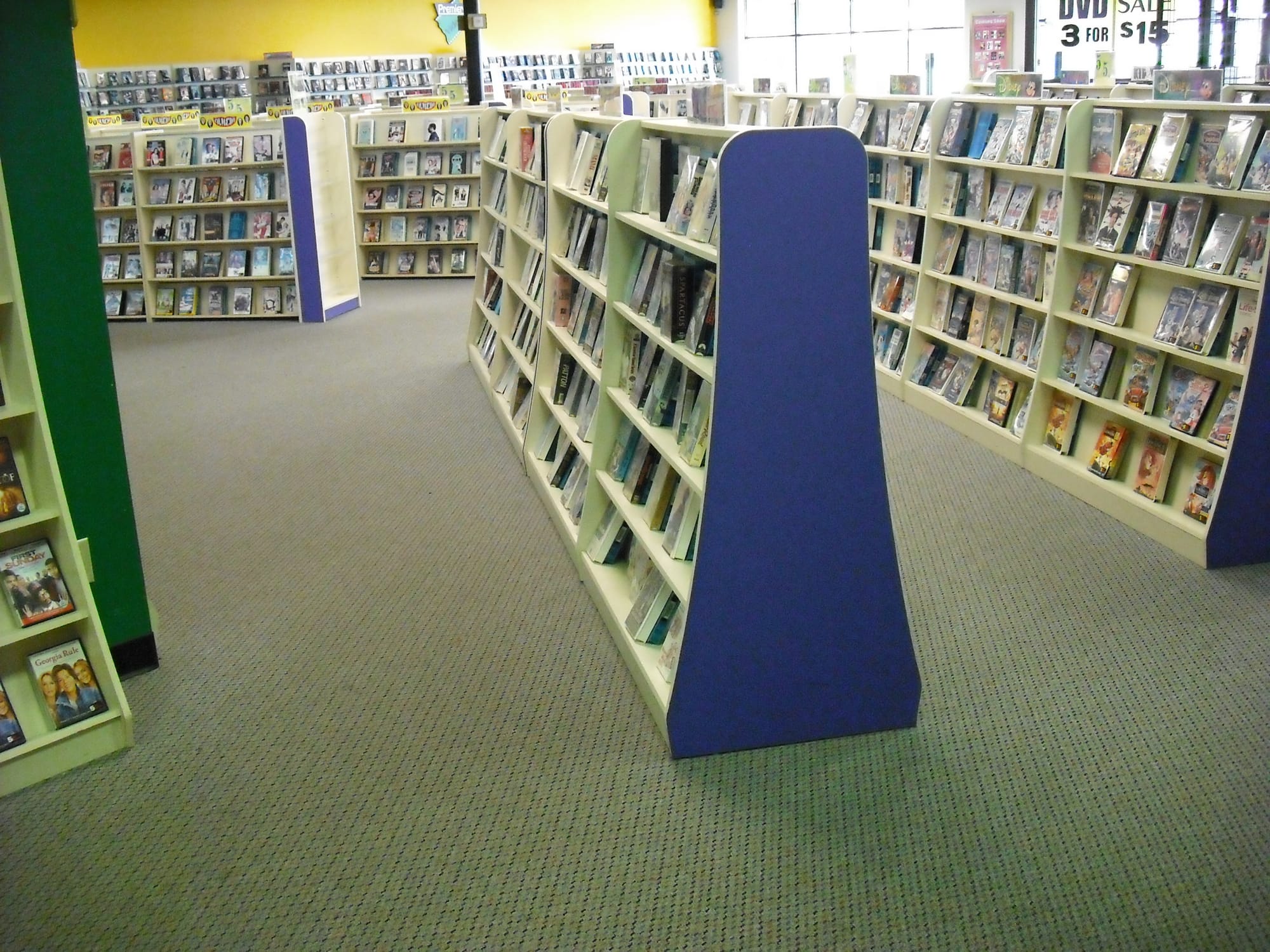 Interior of Premieres Video showing rows of DVD and VHS rental shelves, with movie cases displayed throughout the store and a DVD sale sign near the front window.