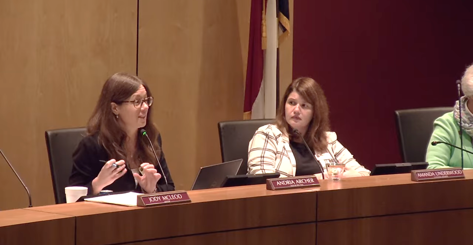 Two women seated behind the Clayton Town Council dais during a public meeting. Andria Archer, identified by the user as seated on the left, speaks into a microphone and gestures with her hands while Amanda Underwood, identified as seated on the right, looks toward her.
