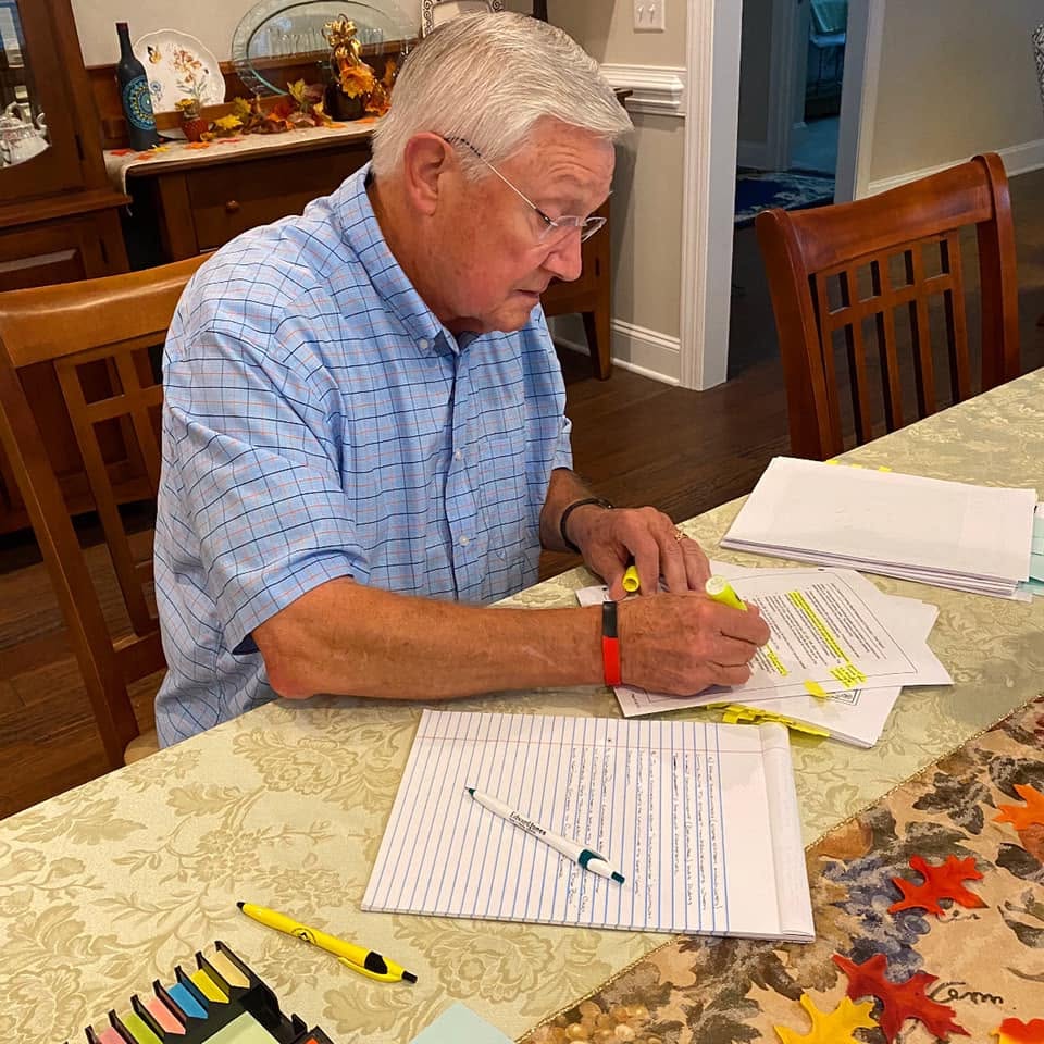 Michael Grannis sits at a dining-room table reviewing and highlighting pages of the Town of Clayton budget, with handwritten notes and documents spread in front of him.