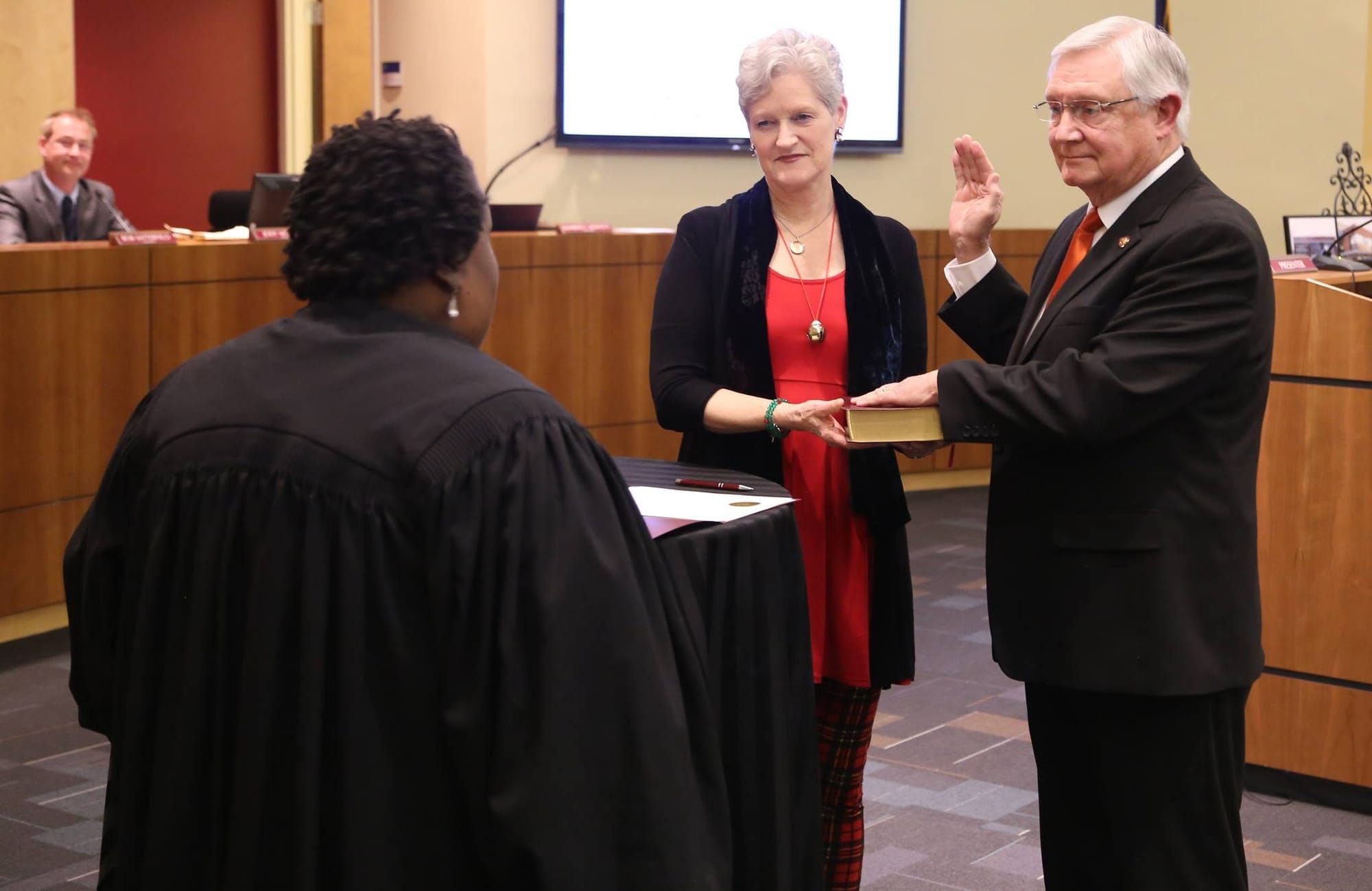 Michael Grannis raises his right hand while being sworn in to the Clayton Town Council as his wife, Betsy, stands beside him holding a Bible.
