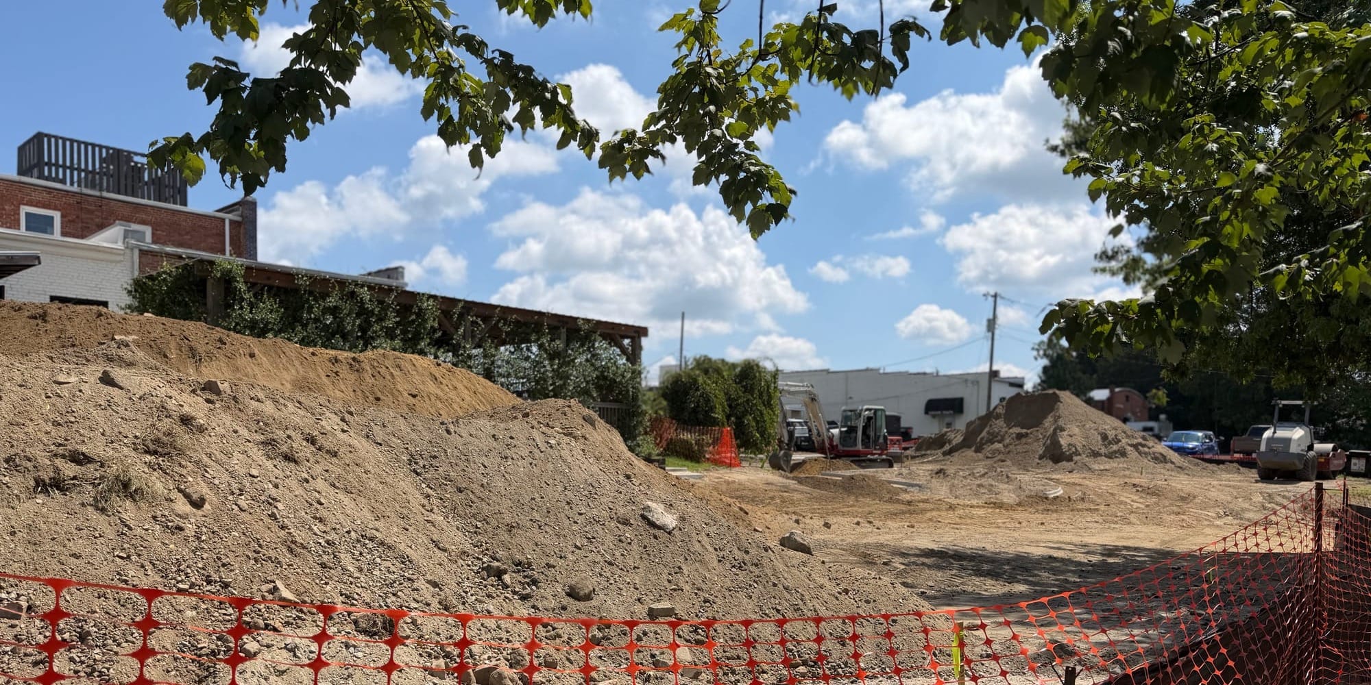 Construction equipment, piles of dirt and orange safety fencing fill the lot behind the Barbour Building in Downtown Clayton as crews prepare the site for paving.