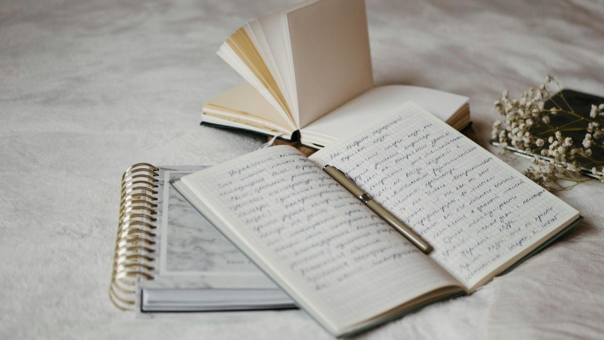 Open notebooks with handwritten poetry and a pen on a soft surface