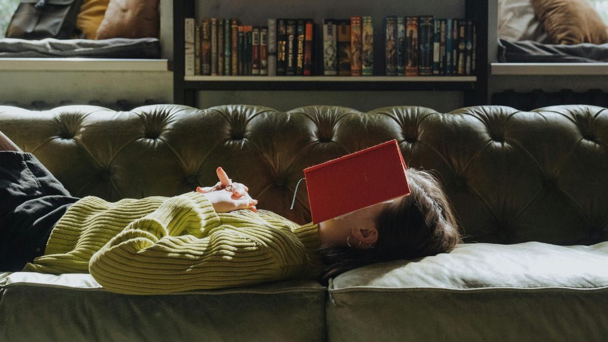 Person relaxing on sofa with face covered by book