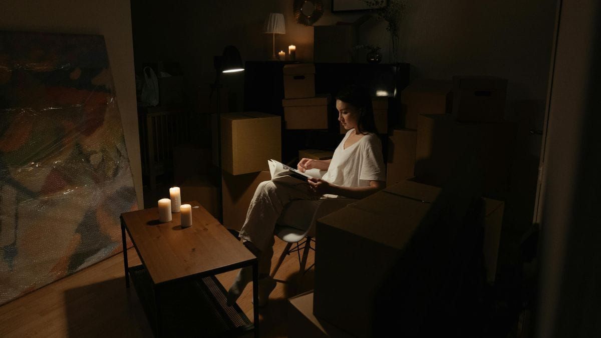 Woman reading a book alone by candlelight surrounded by moving boxes