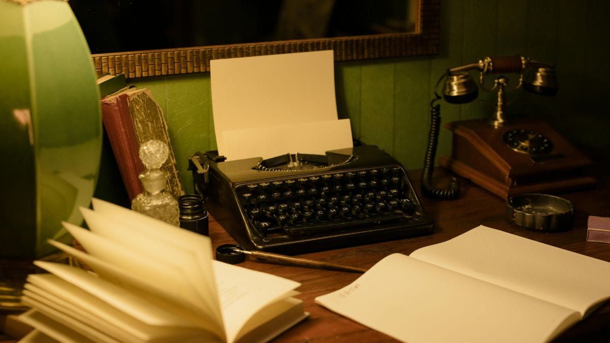 vintage writing setup of typewriter, telephone, and notebook on the table