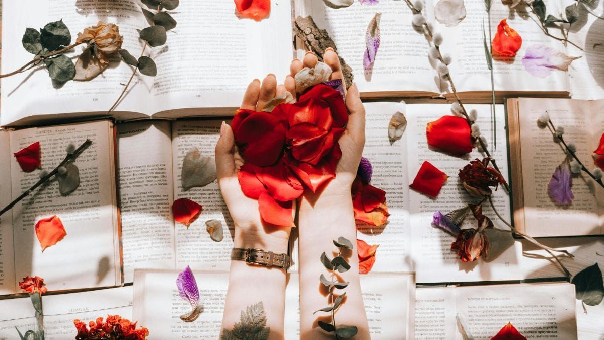 hands with rose petals over books decorated with flowers