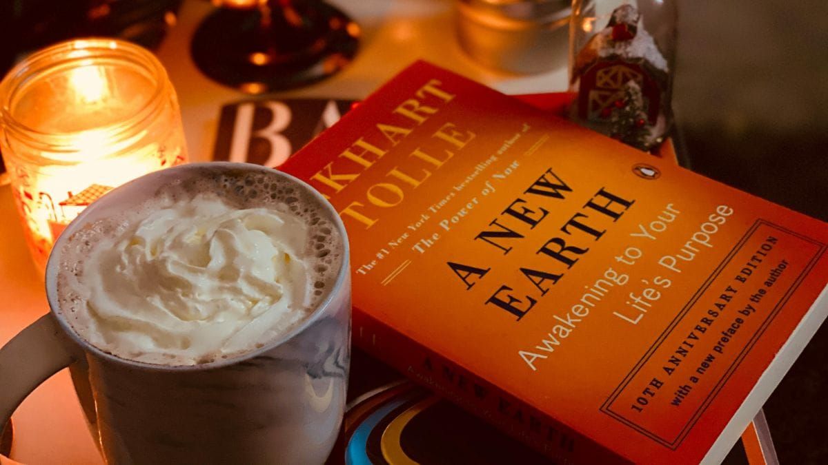 bedside table with a book by Eckhart Tolle, coffee and a candle