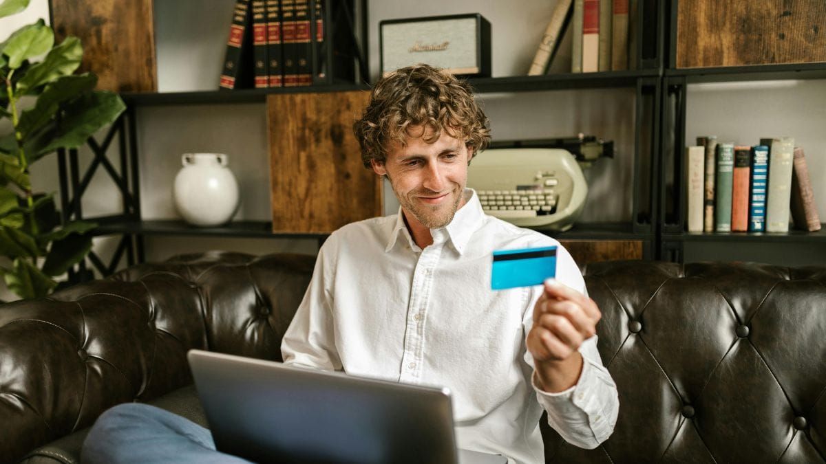 a man smiling at his credit card while sitting with a laptop
