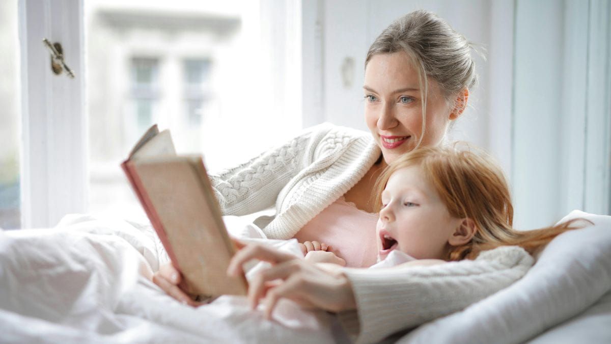 mother and daughter lying in bed and reading a book