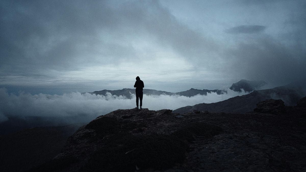 Person standing on mountain top above the clouds at sunrise or sunset.