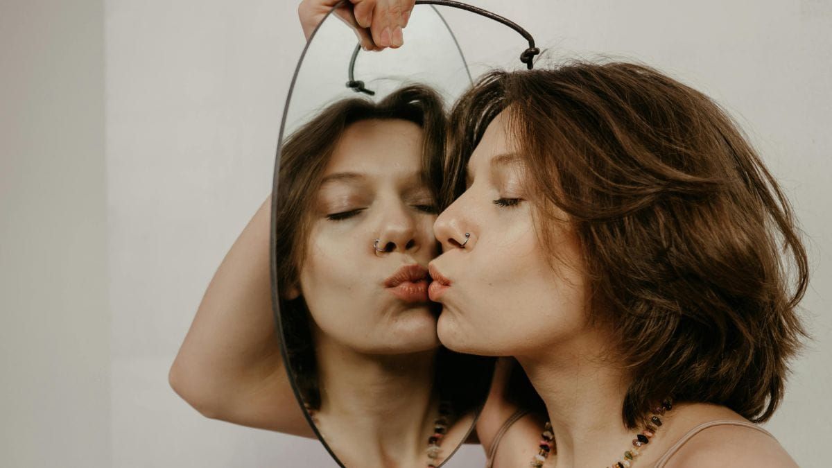 Woman kissing her reflection in a mirror, illustrating themes of self-image and ego.