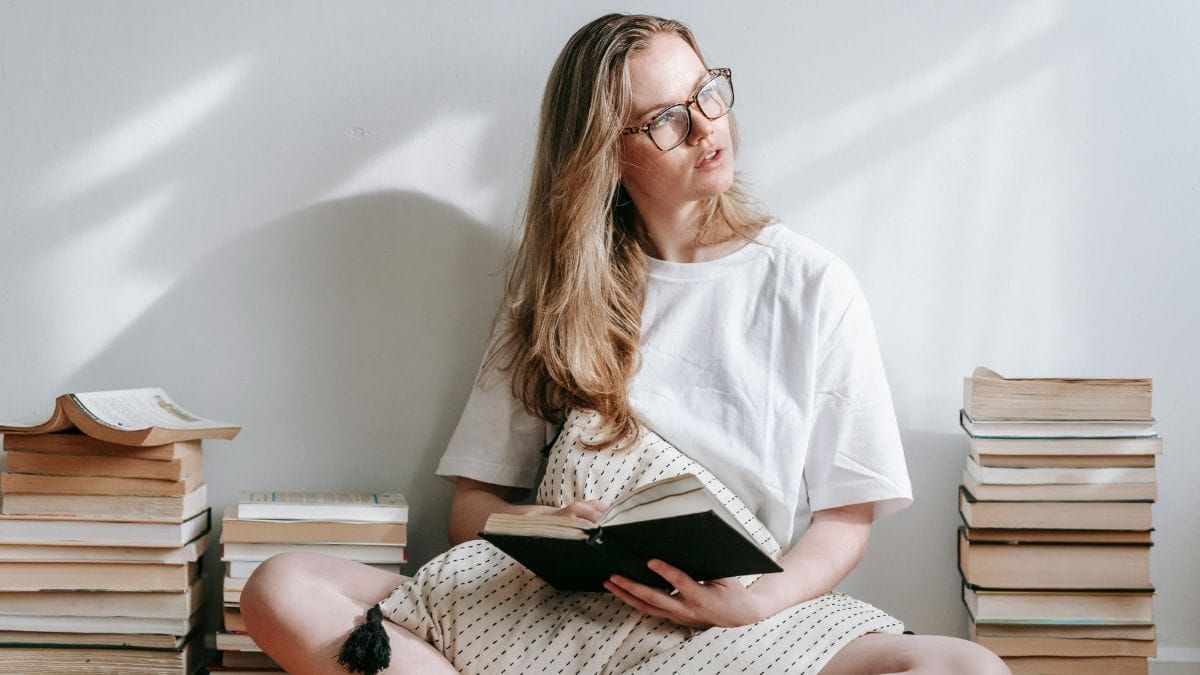 woman reading a book on the floor surrounded by piles of books