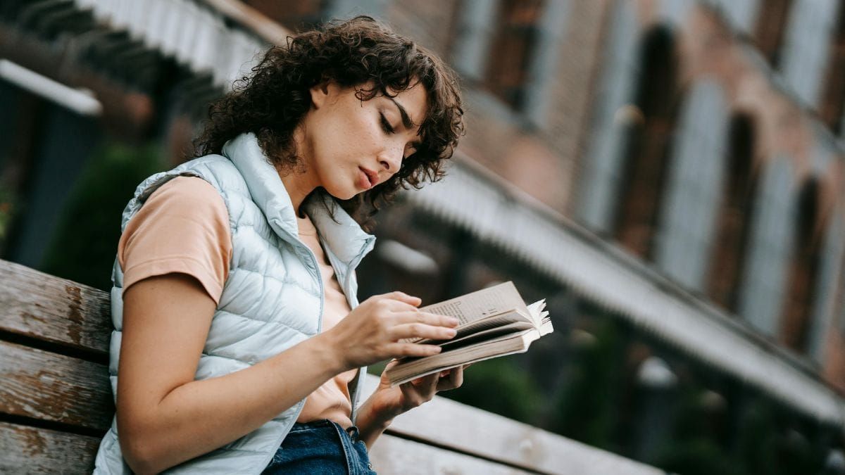 thoughtful young woman reading a book on a bench