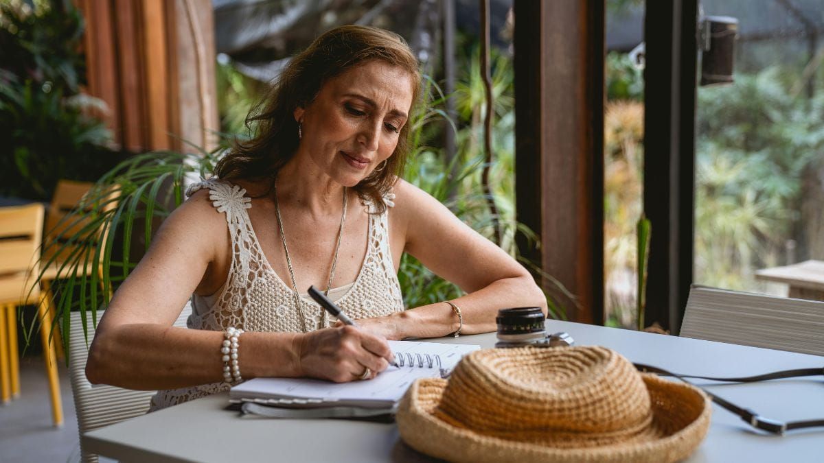 middle-aged woman in travel clothes writing in notebook