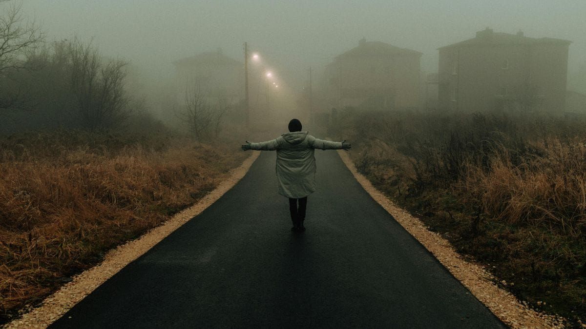 Person standing alone on a foggy road with open arms — symbolizing embodiment and return to visibility.
