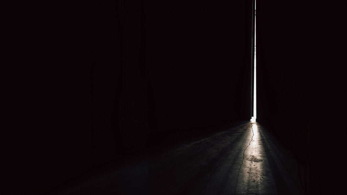 Narrow doorway with a thin line of light in a dark empty space