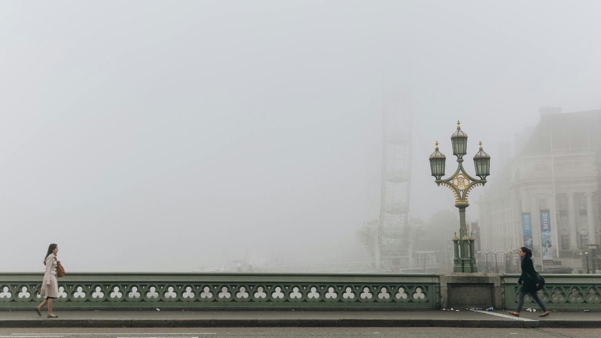 Two people walking in opposite directions on a fog-covered city bridge.