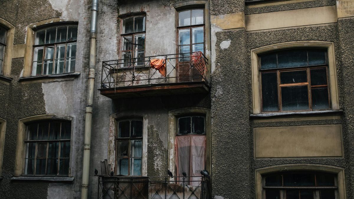 Weathered apartment building facade with cracked walls, old windows, balconies, and pigeons.