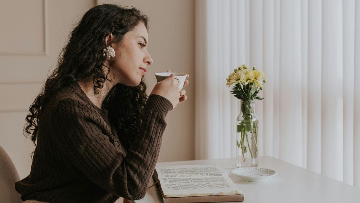 Woman reading by a window with tea and an open book