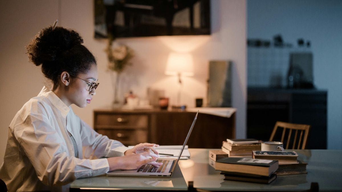 A person working alone on a laptop at night beside books.