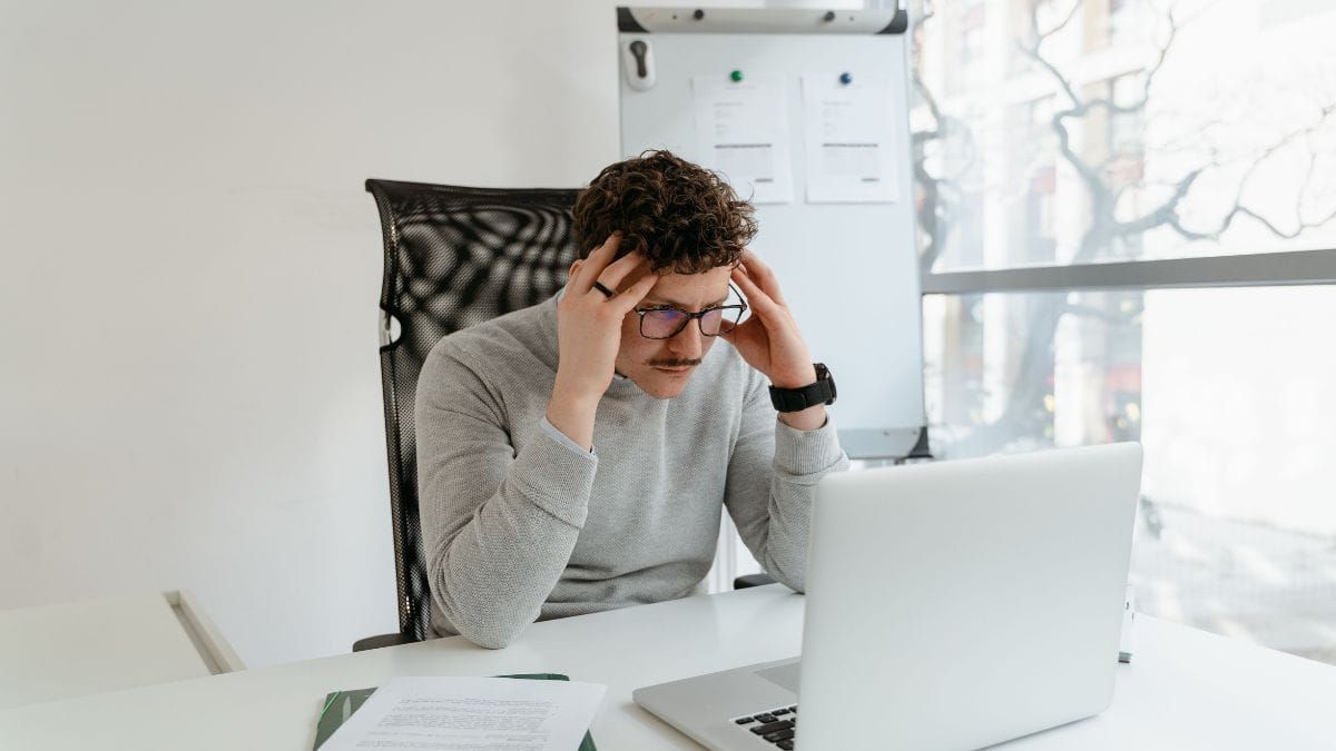 A man looking frustrated while working on a laptop in an office.
