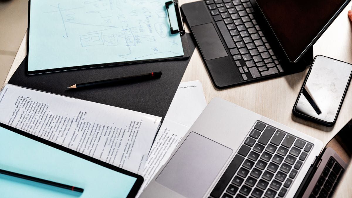 Several laptops, documents, and notes spread across a desk.