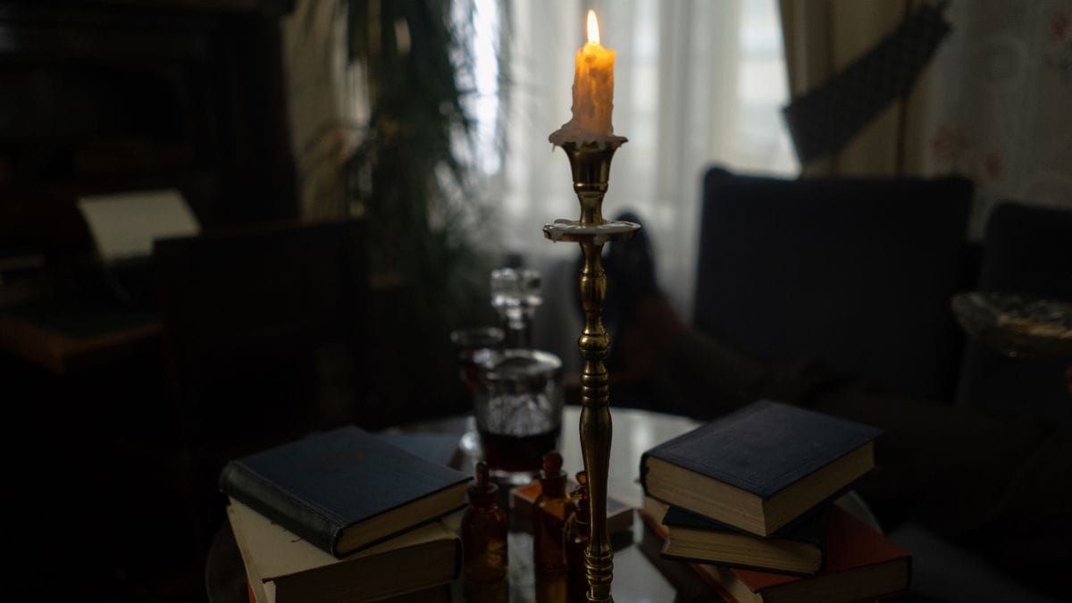 A burning candle surrounded by stacks of books on a table in a dimly lit room.