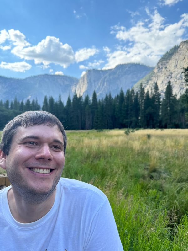 Howard Friedman, a what male with short brown hair, smiles in a field with forest and mountains in the background