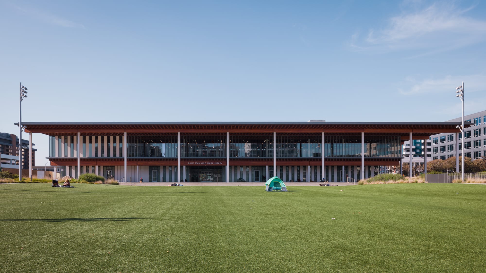 A 1-point perspective view of the Billie Jean King Main Library in Long Beach, California, with homeless tents on the grass in front of the building.