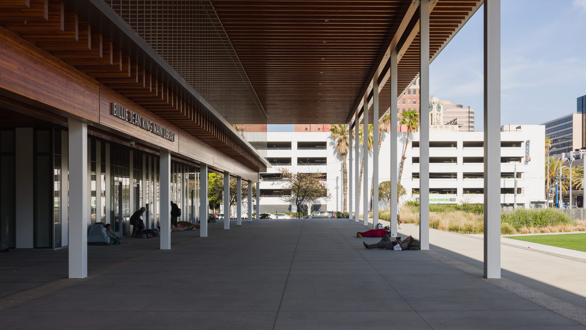 A photo of the overhang in front of the Billie Jean King Main Library in Long Beach, California, with homeless people sleeping in the shade.