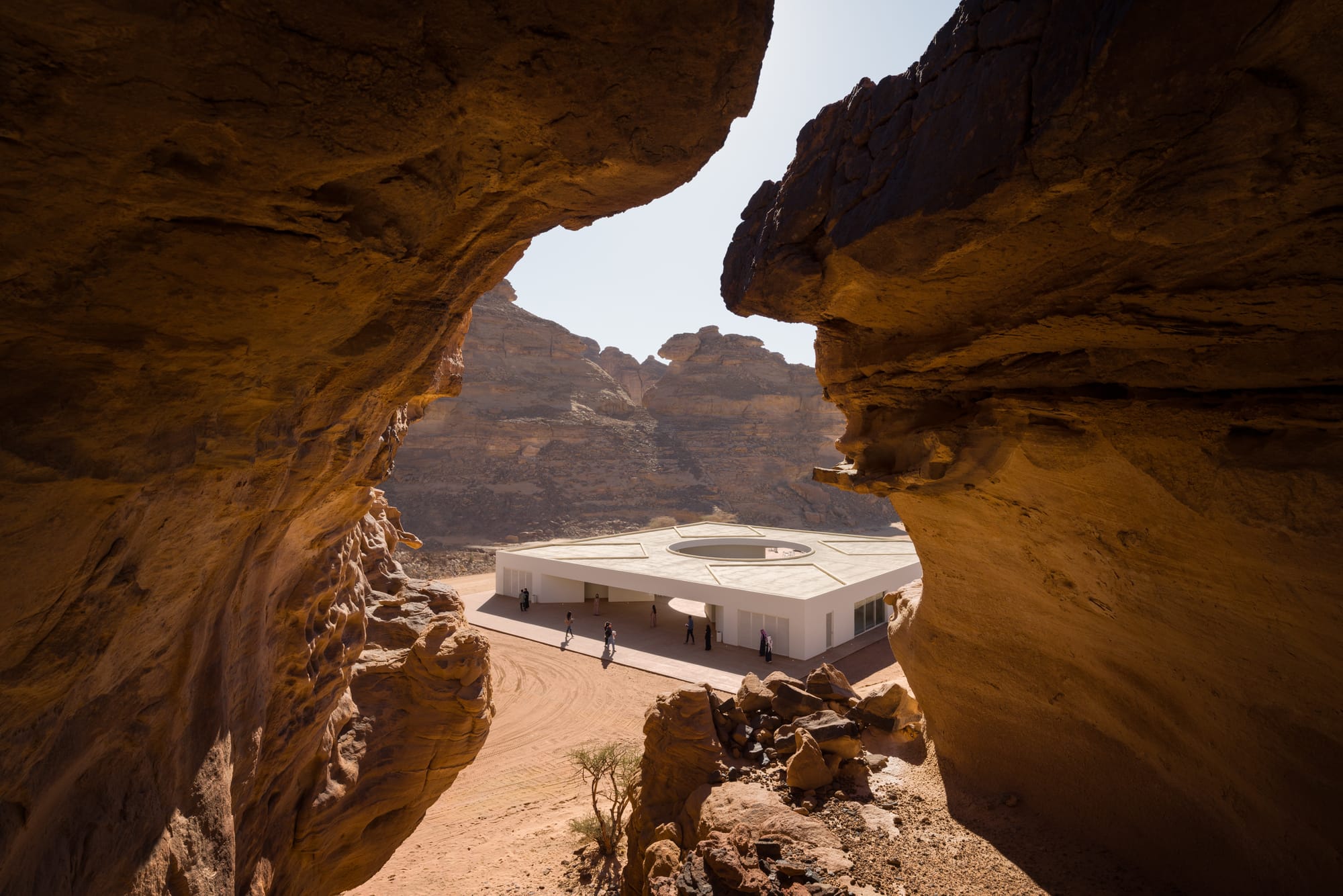 Looking through a rocky crag down onto the Desert X 2024 visitor center in AlUla, Saudi Arabia. Architecture by kwy.studio.