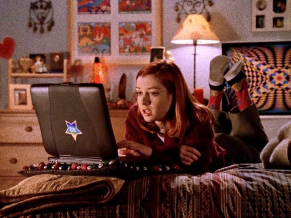 Willow Rosenberg of Buffy lays on her stomach in front of a laptop of the 90s.