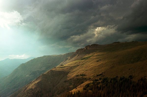A dramatically lit image of storm clouds forming over a mountain ridge in Rocky Mountain National Park. The air is smokey, giving the scene a muted, ominous feeling.