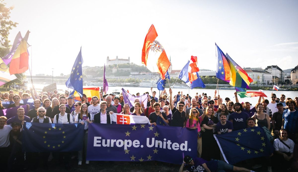 Members of Volt Europa after the general assembly in Bratislava in June 2026 waving flags from european countries, the EU flag and pride flags. Standing in front of the river danube.
