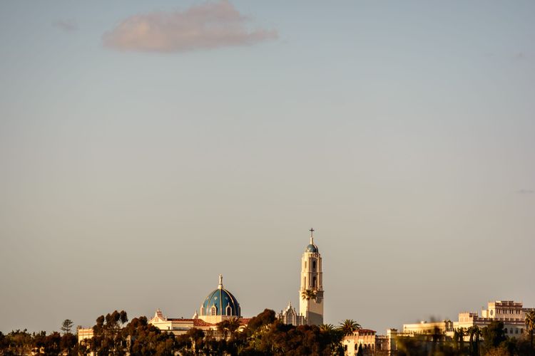mostly a grayish sky with a solitary wispy cloud at the top of the frame, the bottom eighth of the image is a few buildings of the University of San Diego from a distance