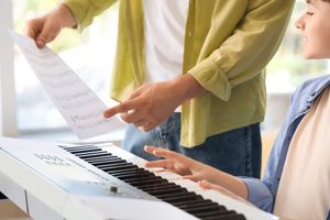 Piano teacher handing sheet music to a student at a keyboard, illustrating how music educators choose between free and licensed sheet music