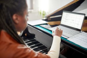 Pianist viewing sheet music on a laptop at a piano, comparing free and licensed sheet music options online