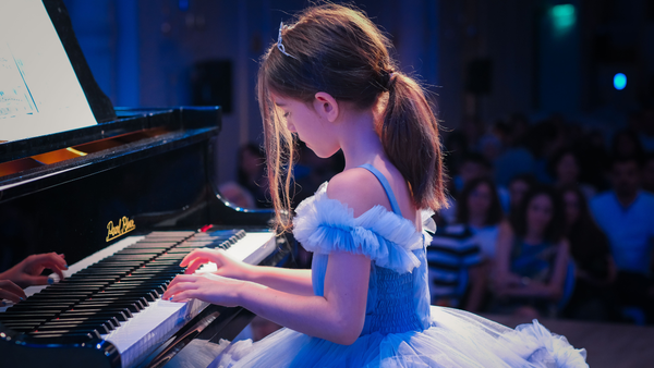 Beginner piano student playing piano with sheet music at piano recital. Photo by Emre Gokceoglu
