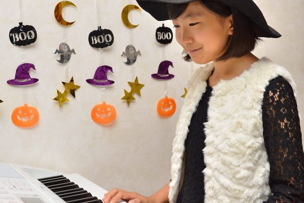 child with witches hat playing piano. halloween decor on wall
