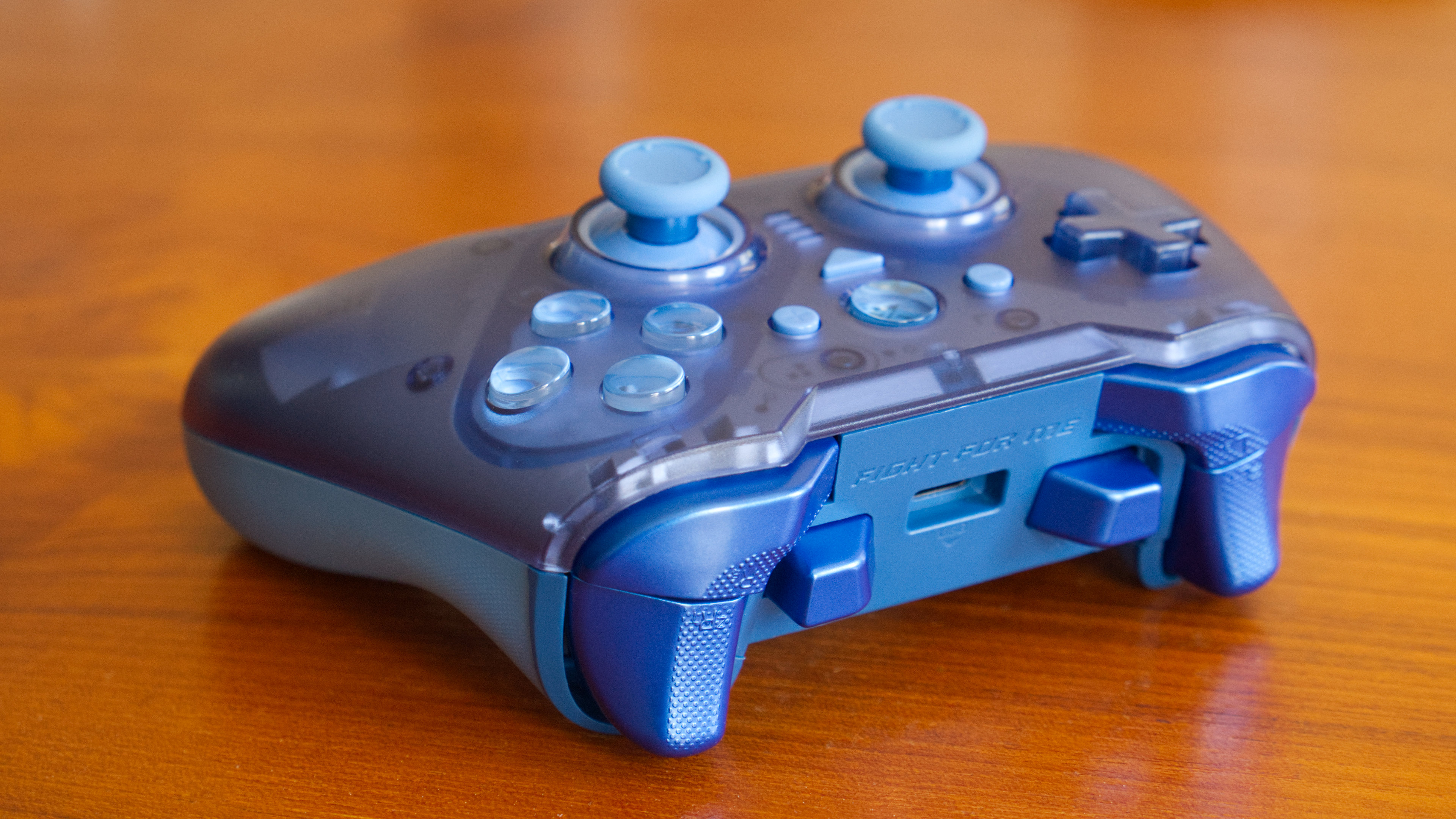 The ZD-O+ Excellence controller in blue on a wood backdrop, as seen from the side profile. "Fight For Me" is shown on the sides, and it has 3 sets of triggers.